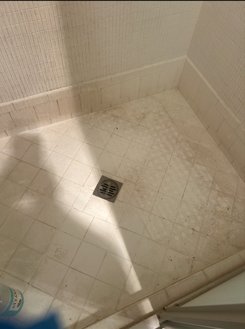 Stained tile shower floor with dirty grout before cleaning