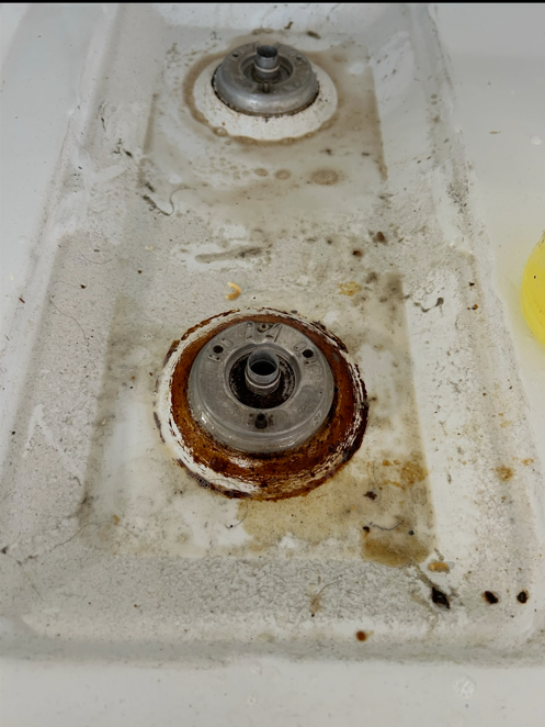 Grease and rust buildup around a gas stove burner before cleaning